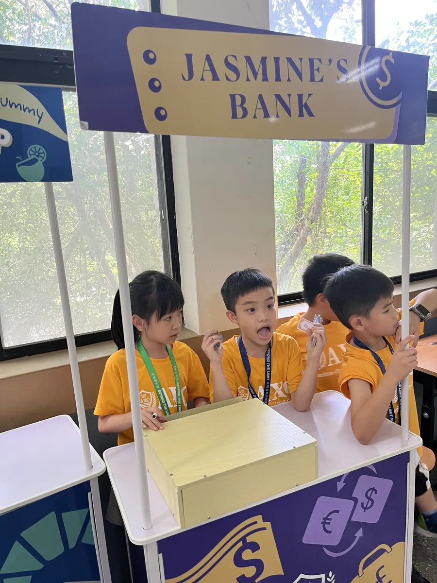 孩子在教室裡經營招牌寫著「Jasmine's Bank」的銀行攤位